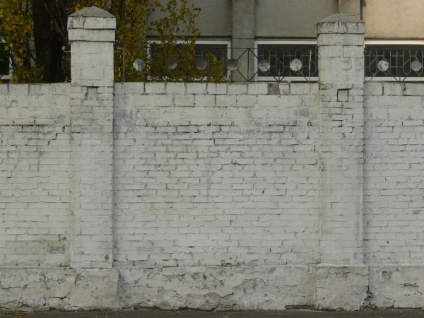 Brick fence texture made up of bricks painted white, with two tall columns made up of similar bricks. Bricks are in various degrees of relief and states of erosion.